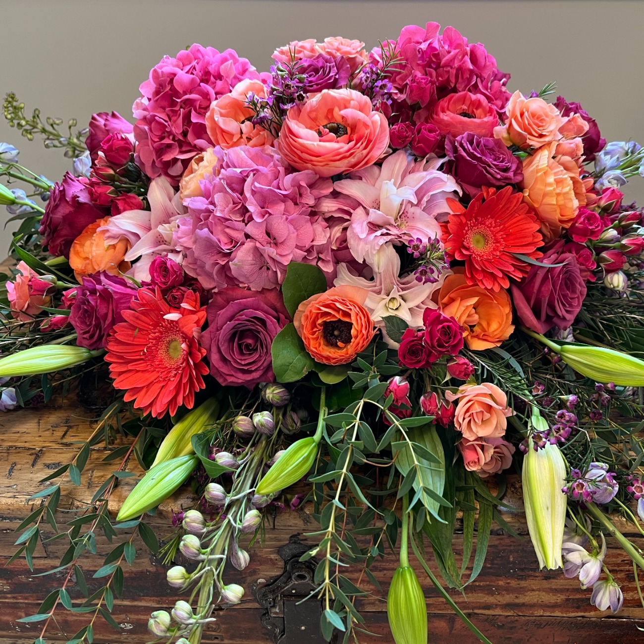 Low arrangement of hydrangea, ranunculus, gerbera and delphinium on a wooden chest