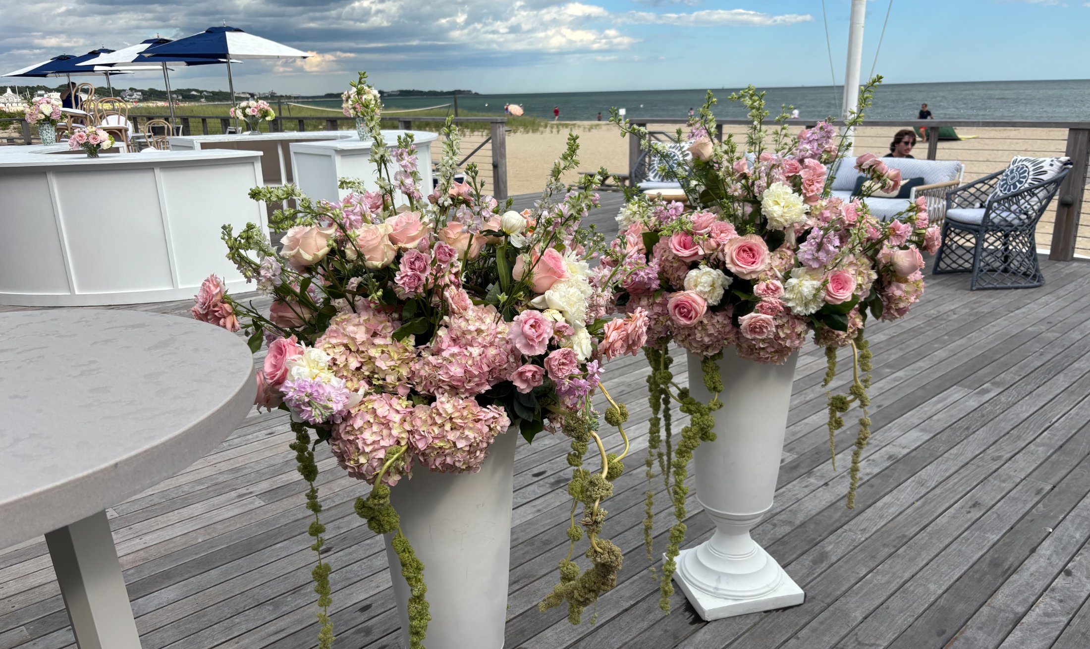 Blush urn arrangements on a deck above the beach