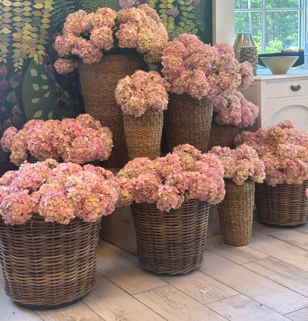 Baskets of pink hydrangea gathered in the shop against the painted floral mural